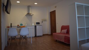 A compact living space with a kitchenette, a dining area with two chairs, a red sofa, and a white shelving unit. - Studio Penthouse La Casa de Manuel, is located in Portomarín, 22km from Sarria. (Portomarín)