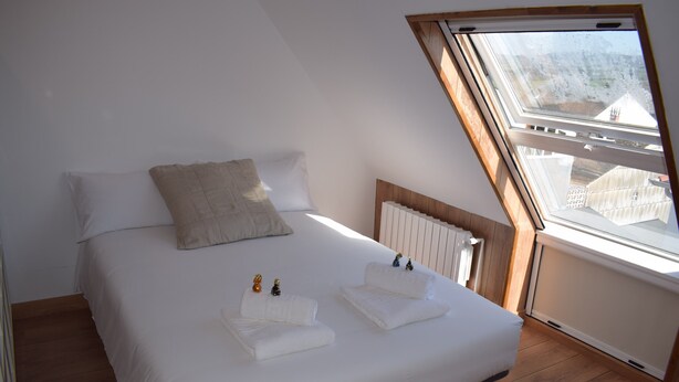 A bedroom with a sloped ceiling, a bed with white linens, a radiator, and a view through a window. - Studio Penthouse La Casa de Manuel, is located in Portomarín, 22km from Sarria. (Portomarín)