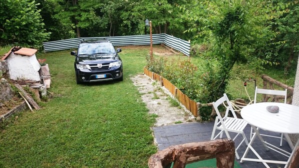 A black car parked in a grassy backyard with a white fence, a stone pathway, and a white table with chairs.