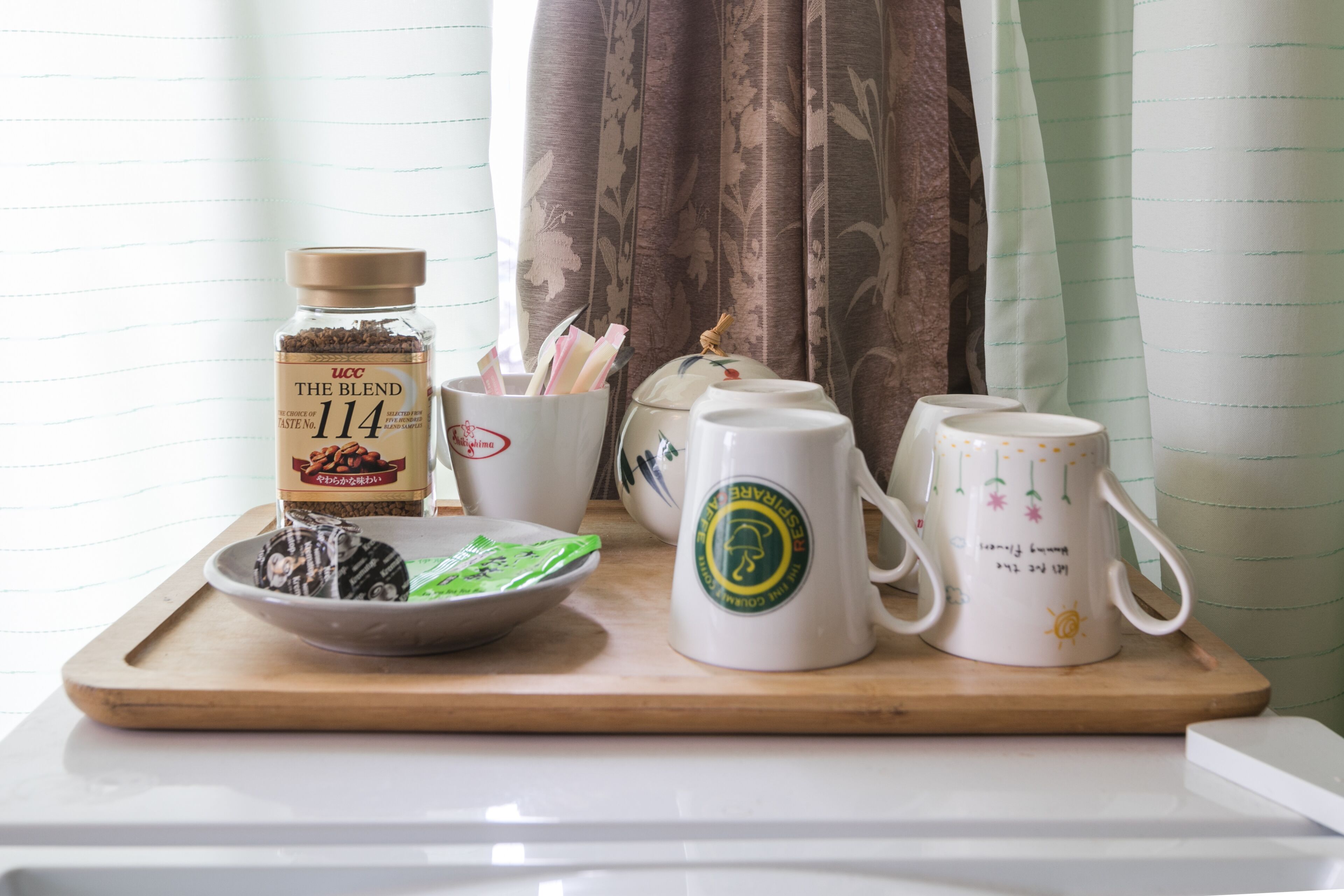A tray with a tea bag, a jar labeled "UCC The Blend 114," and several white mugs with floral designs.