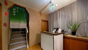 Une chambre d’hôtel avec un escalier en bois, une petite kitchenette, un comptoir de réception et une plante en pot.