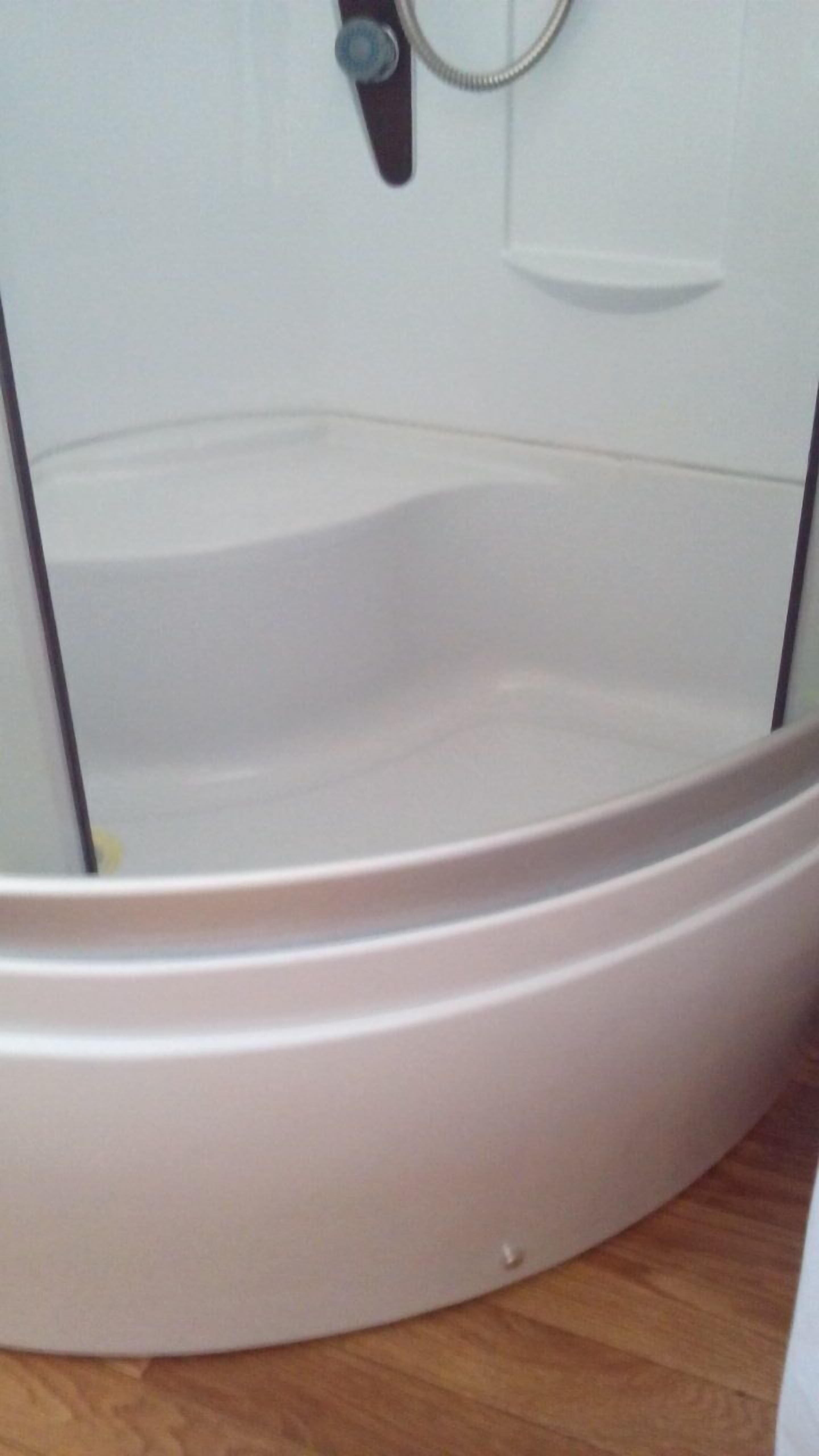 Una bañera blanca de diseño curvo, una ducha y una pequeña llave de control.