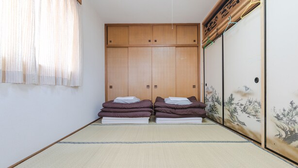 Une pièce de style japonais traditionnel, avec un sol recouvert de tatamis, une porte coulissante ornée d’œuvres d’art et un lit recouvert de couvertures pliées.
