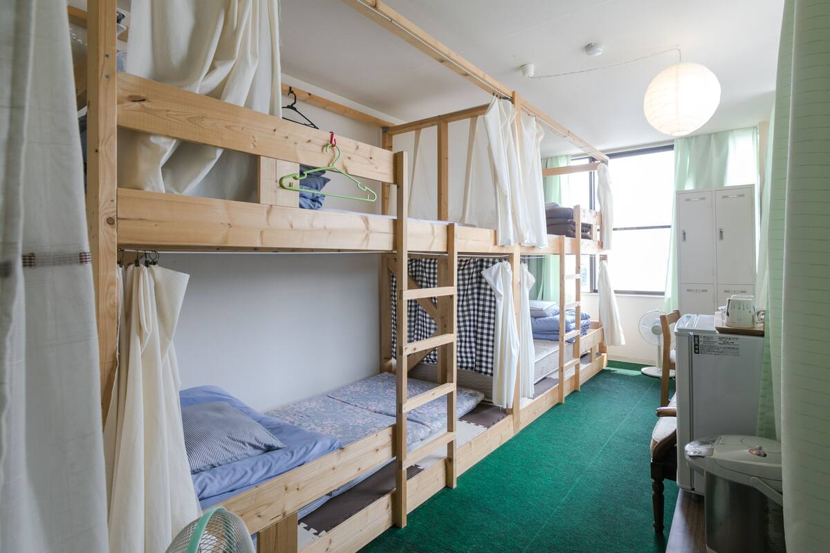 Une chambre avec un lit superposé en bois, un ventilateur et une petite kitchenette.