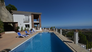 A swimming pool with lounge chairs, a building with a balcony, and a view of the sea. - Villa with stunning panoramic views to the sea, privacy and swimming pool (Mijas)