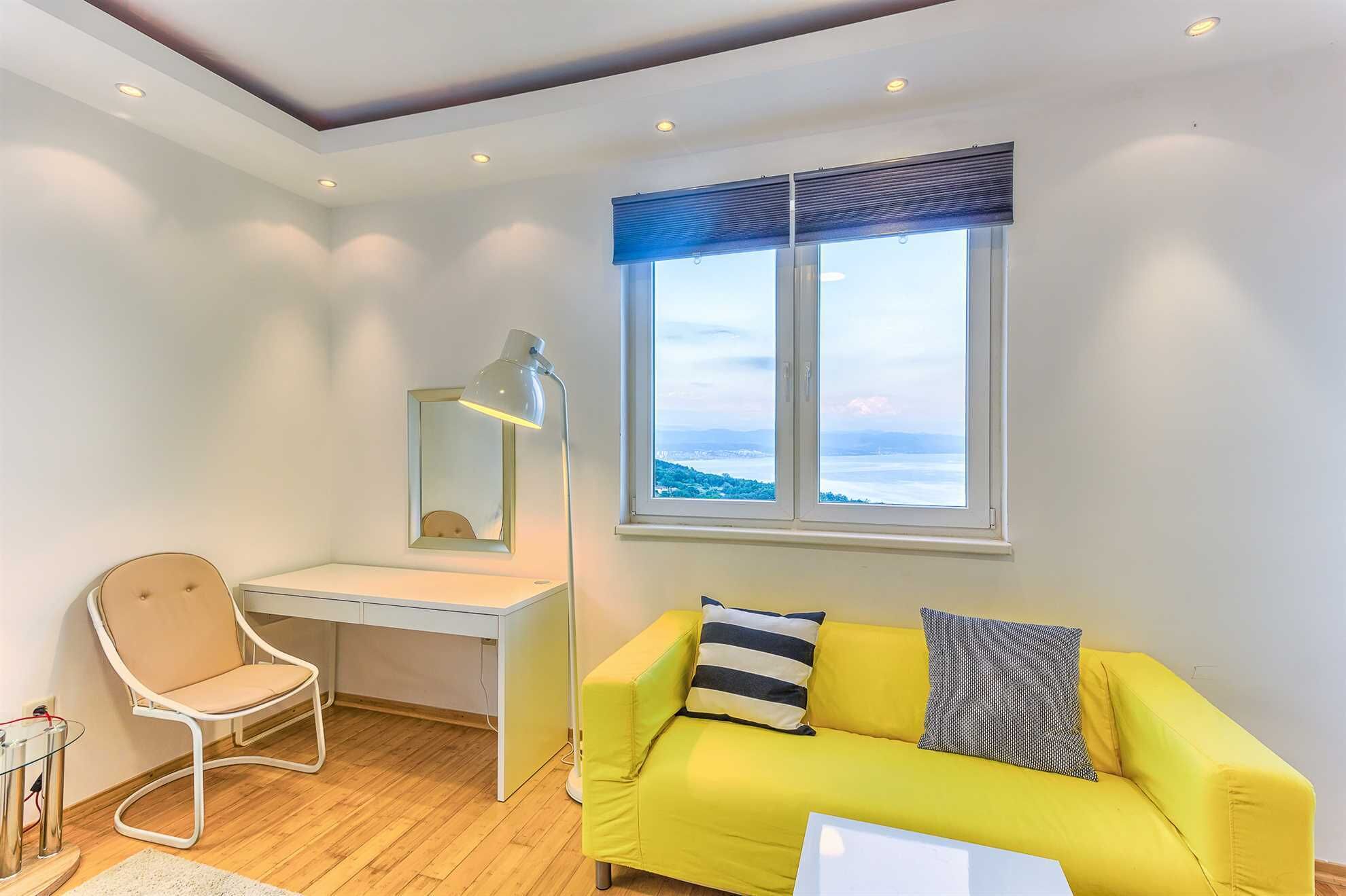 A bright room with a yellow sofa, a desk, and a large window with a view.