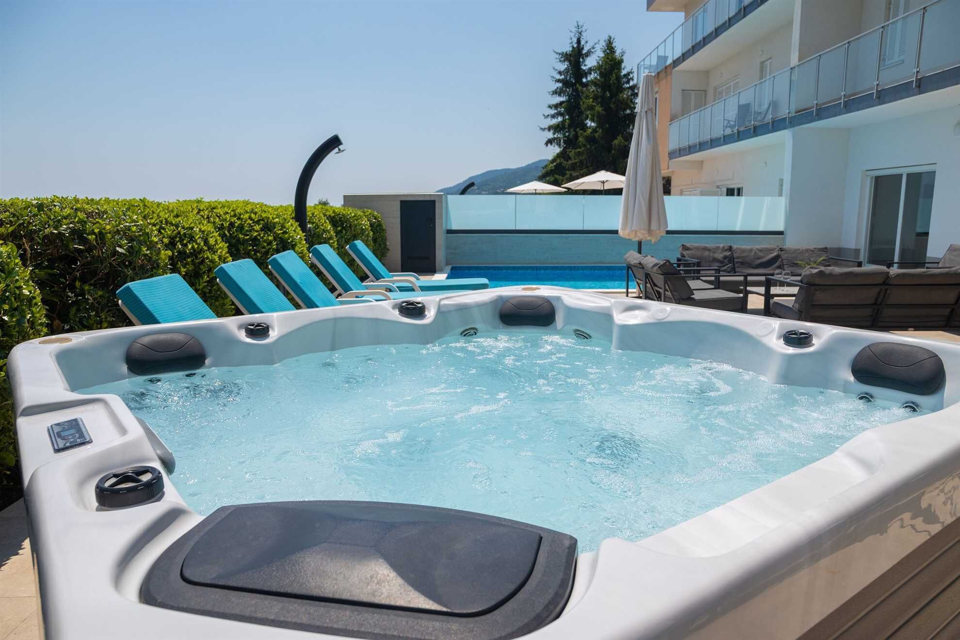Un jacuzzi con sillones de descanso, una piscina y un edificio con balcones al fondo.