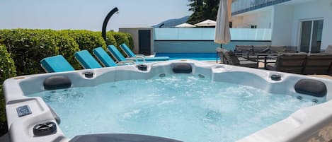 A hot tub with lounge chairs, a pool, and a building with balconies in the background.