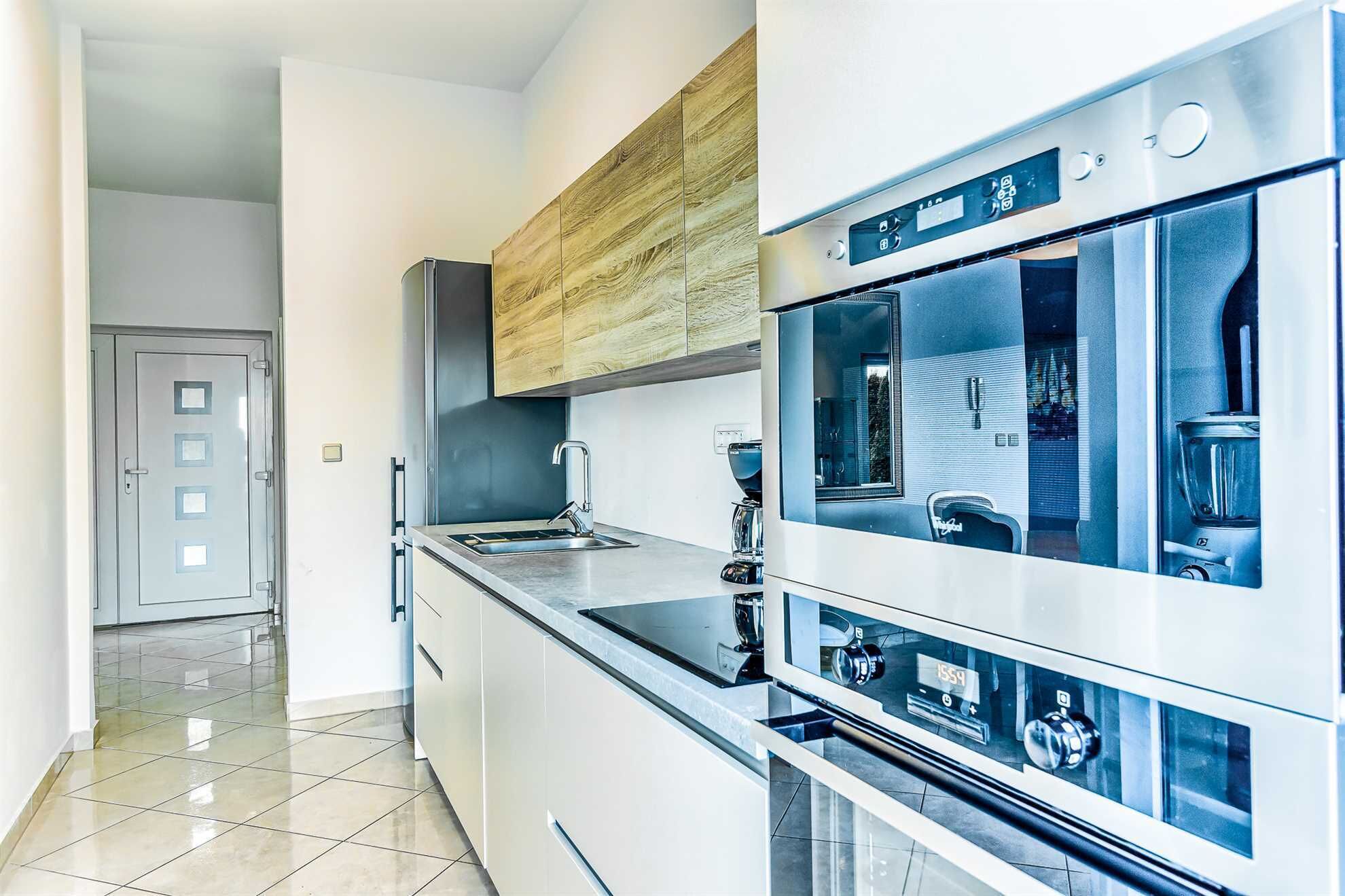 Une cuisine moderne dotée d’appareils électroménagers en acier inoxydable, d’un meuble supérieur en bois et d’un sol carrelé.