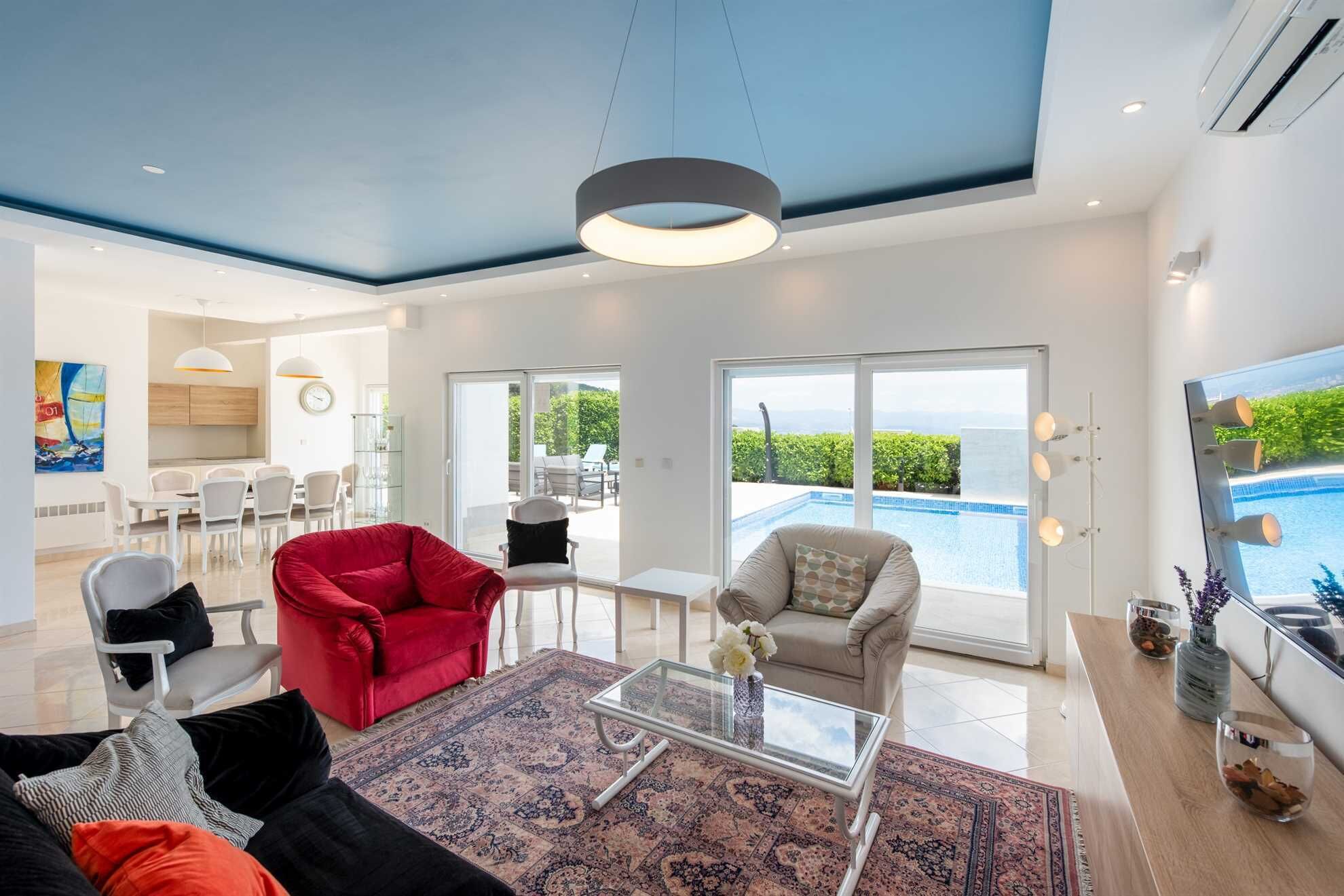A spacious living area with a red sofa, a glass coffee table, and a view of a swimming pool.
