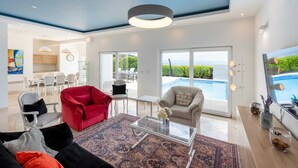 A spacious living area with a red sofa, a glass coffee table, and a view of a swimming pool. - Villa Sole - five bedrooms with sea views and a private pool by MyWaycation (Poljane)