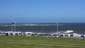 Vista costera con una hilera de cabañas de playa, una zona verde y el océano.