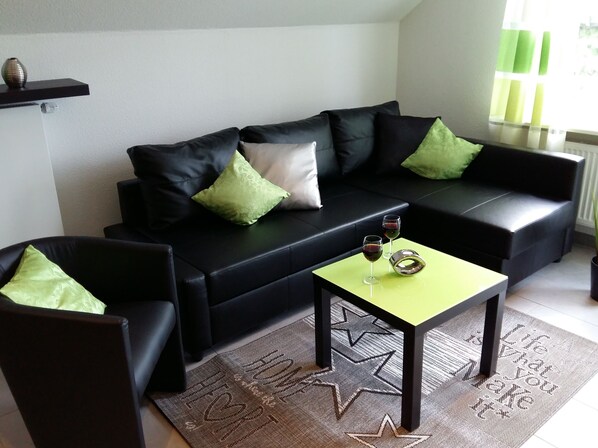 A modern living room with a black sofa, two green pillows, a yellow coffee table, and two wine glasses. - Self-in Goslar, suitor Apartments - Attic (Goslar)
