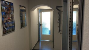 Un pasillo con suelo de baldosas, una puerta que da a una habitación luminosa y un cuadro en la pared.