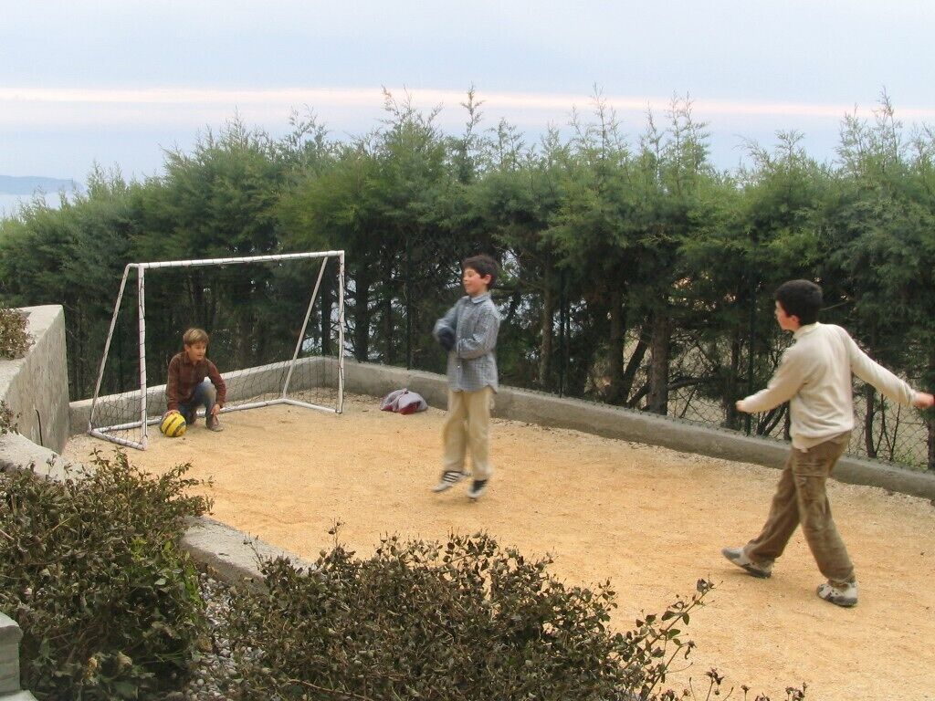 A sandy outdoor area with a goalpost, surrounded by greenery.