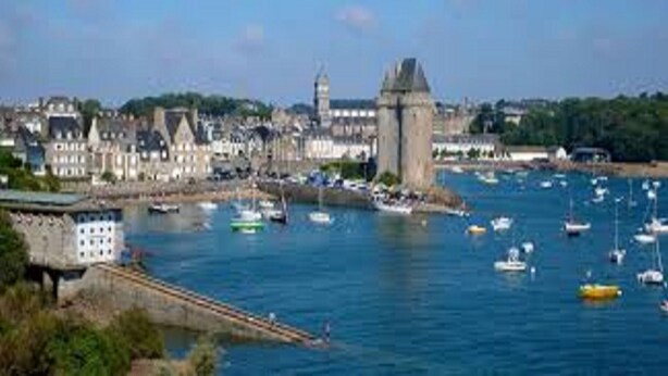 A coastal town with a prominent tower, a marina with boats, and a mix of historic and modern buildings.