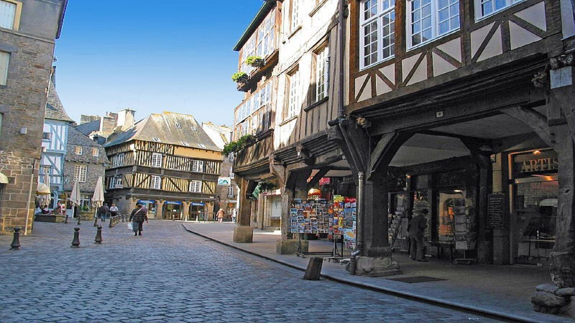 A cobblestone street lined with traditional half-timbered buildings, a bookshop, and a café.