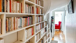 A library with bookshelves filled with books, a red chair, and a television on the wall. - HISTORIC CENTER St. Germain-Près—close to the metro, the river, shopping, comfortable, quiet, and bright (Paris)