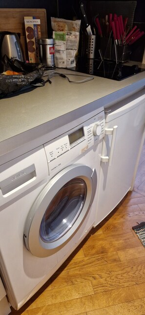 A front-loading Siemens washing machine with a control panel, a wooden countertop, and various kitchen items.