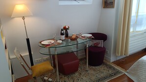 A dining area with a glass table set for two, a red chair, a yellow chair, a lamp, and a window with curtains. - HISTORIC CENTER St. Germain-Près—close to the metro, the river, shopping, comfortable, quiet, and bright (Paris)