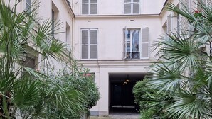 A courtyard with a tiled floor, potted plants, and a building with multiple windows and shutters. - HISTORIC CENTER St. Germain-Près—close to the metro, the river, shopping, comfortable, quiet, and bright (Paris)
