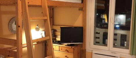 Habitación con literas, televisión, cajones, una mesita y ventana.
