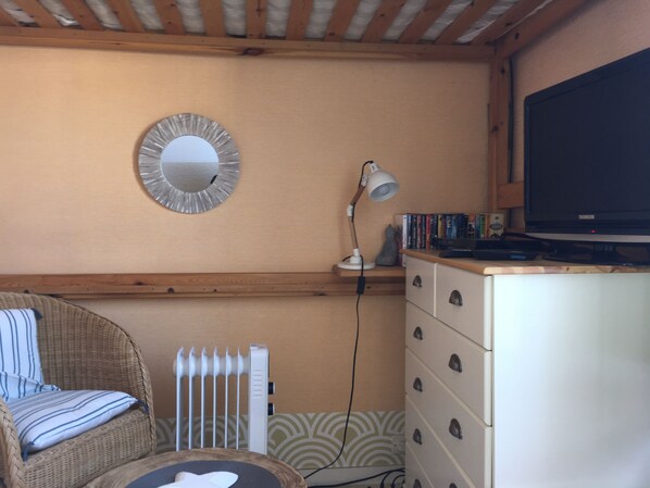 Een gezellige kamer met een rieten stoel, een witte dressoir, een spiegel, een lamp en een televisie.
