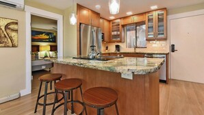 A modern kitchen with a large island, wooden cabinets, and pendant lighting. - Family Getaway 3BD Across from  Beach-Pacific Shores B102 (Kihei)