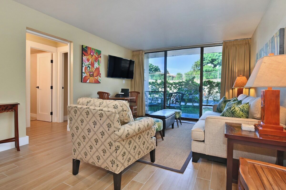 A living room with a sofa, a TV, a coffee table, and a view of the outdoors.
