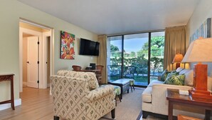 A living room with a sofa, a TV, a coffee table, and a view of the outdoors. - Family Getaway 3BD Across from  Beach-Pacific Shores B102 (Kihei)
