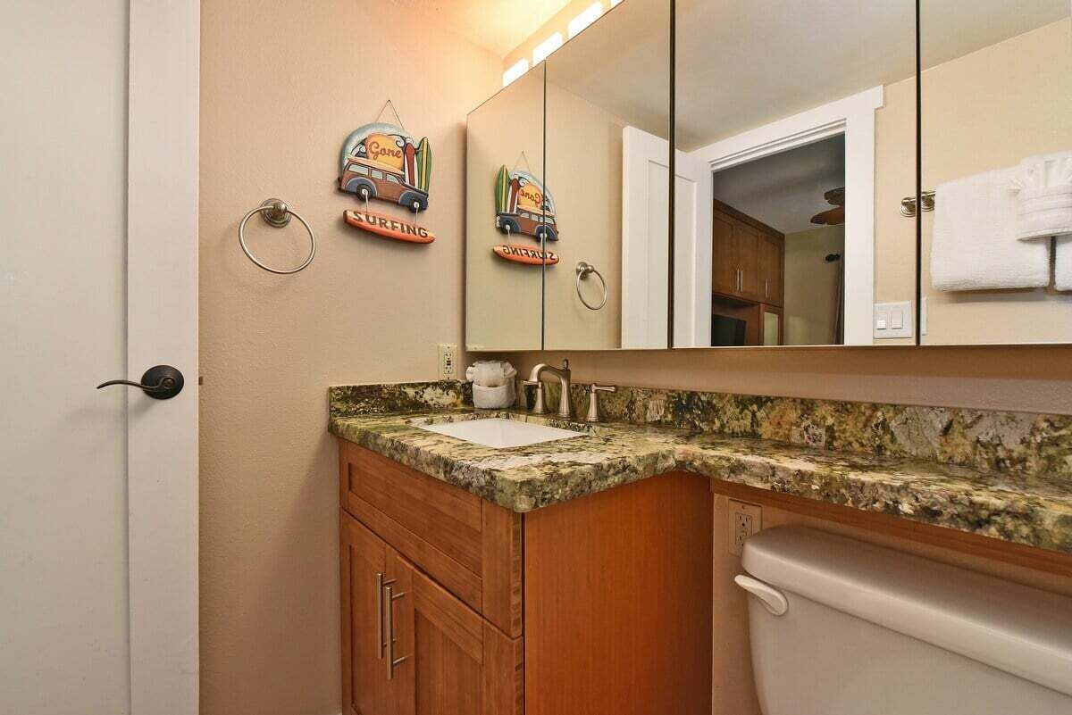 A bathroom with a granite countertop sink, wooden cabinets, and a toilet.