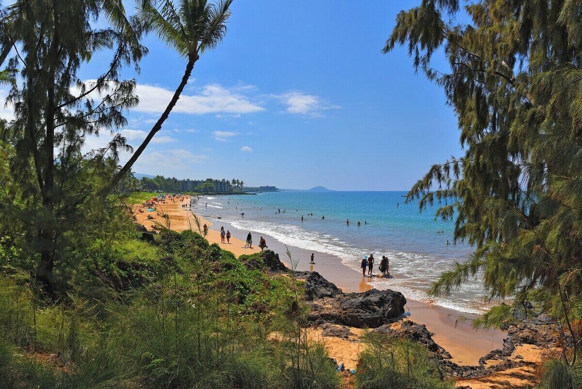 Una playa con agua azul cristalina, gente nadando y un litoral rocoso.