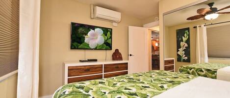 A bedroom with a bed, a television, a dresser, and a ceiling fan.