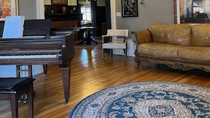 Un vaste salon agrémenté d’un magnifique piano à queue, d’un canapé en cuir, d’un tapis à motifs et d’un lustre.
