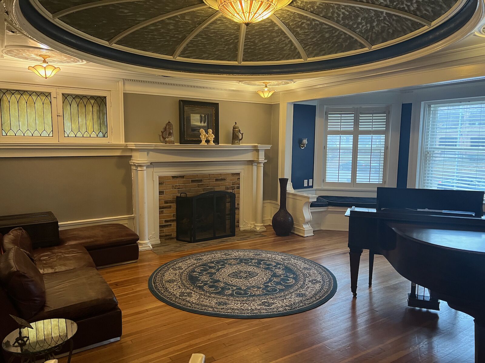 A living room with a fireplace, a piano, a round rug, and a ceiling with a skylight.