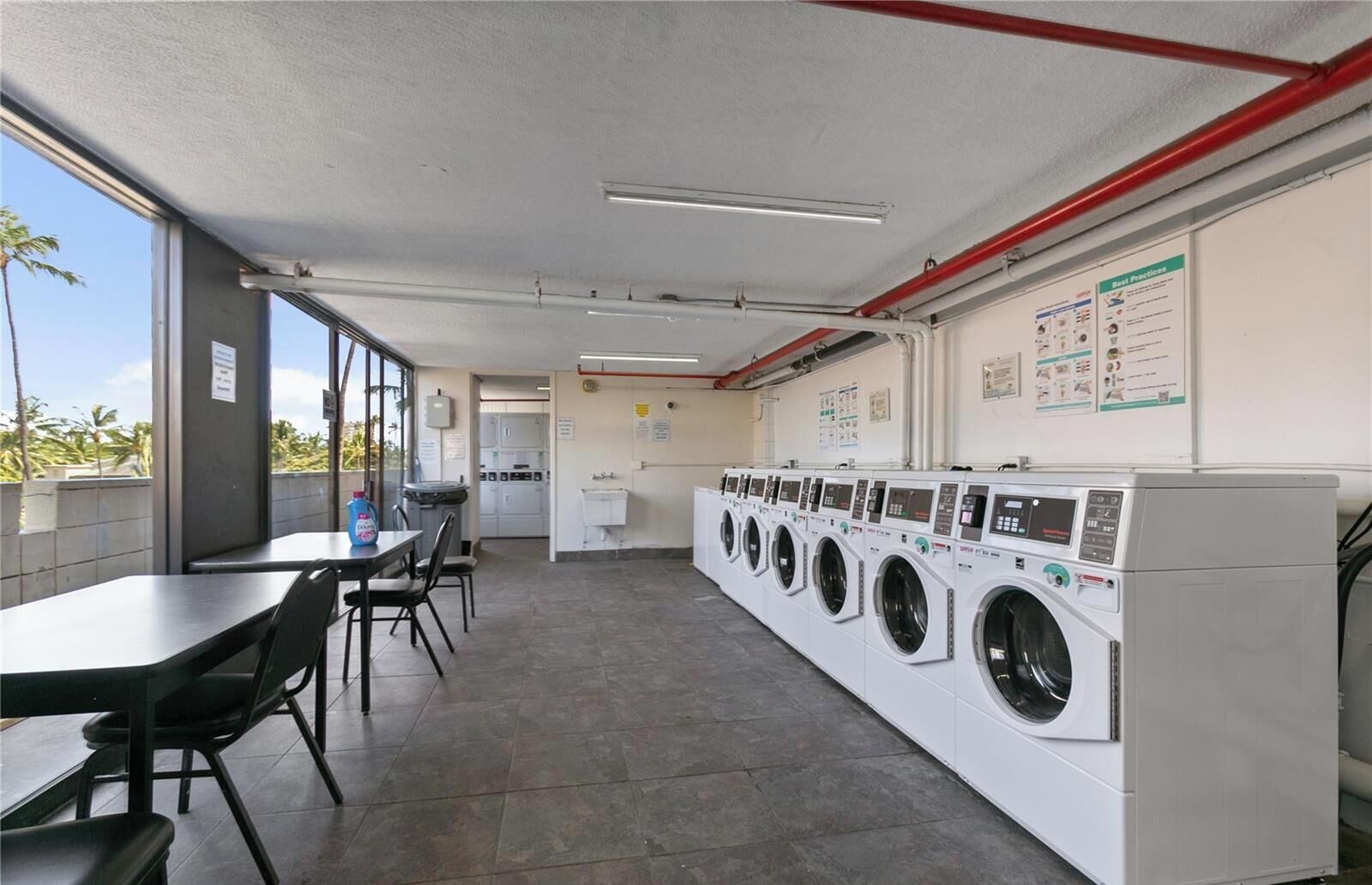 Una lavanderia self-service con diverse lavatrici, un tavolo con sedie e vista sull'esterno.