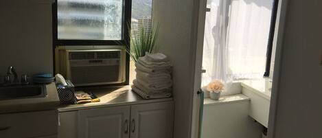 A small kitchen with a window, a sink, and a stack of towels.