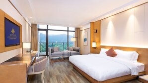 A hotel room with a large bed, a desk, a sofa, and a TV. There is a view of mountains through the window. - Minyoun Langzhong Ancient City Resort (Nanchong)