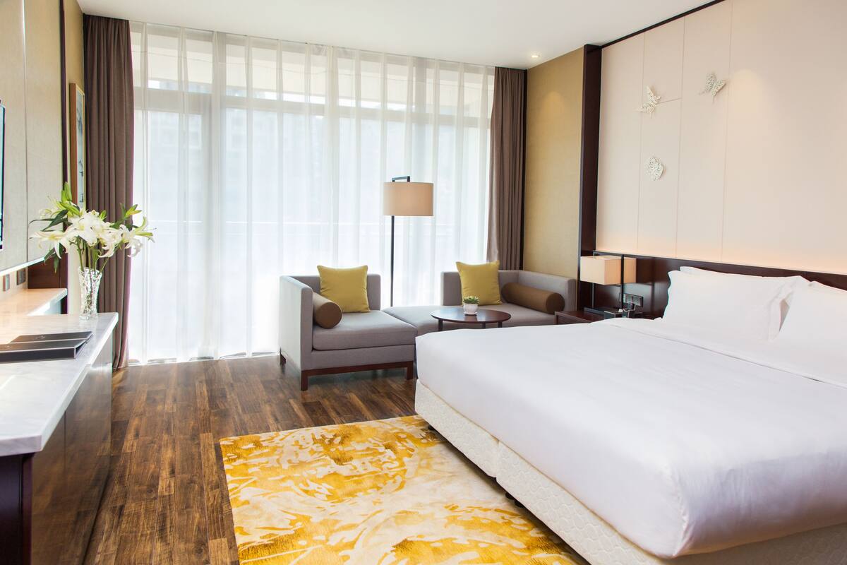 A hotel room with a large bed, a sofa, a desk, and a lamp.