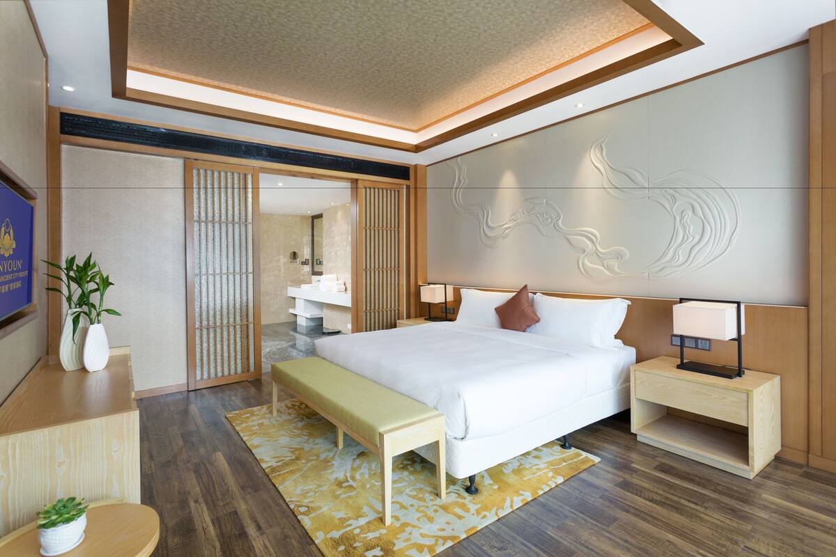A modern hotel room with a large bed, bedside tables, a bench, and a decorative wall.