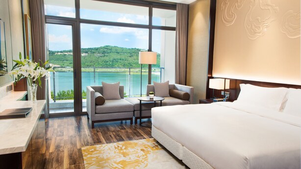A hotel room with a large bed, a sofa, a small table, and a view of a lake and hills. - Minyoun Langzhong Ancient City Resort (Nanchong)