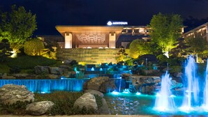 A hotel with a waterfall feature in the foreground and a well-lit building in the background. - Minyoun Langzhong Ancient City Resort (Nanchong)