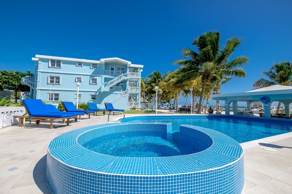 A swimming pool with blue tiled edges, lounge chairs, and a multi-story building with balconies.