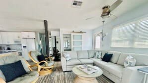 Ein modernes Wohnzimmer mit grauem Sofa, Korbstühlen, einem Couchtisch und einer Küche im Hintergrund.