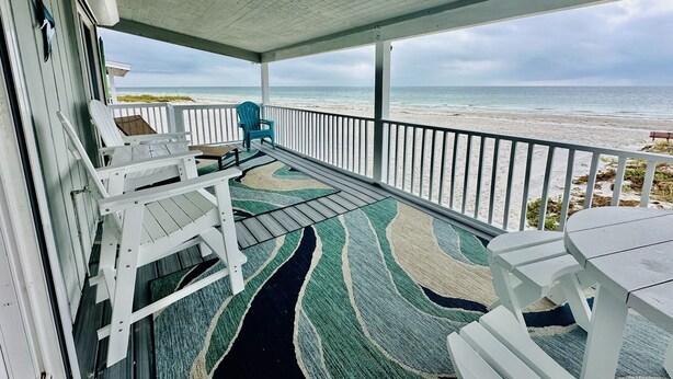 Eine überdachte Veranda mit weißen Geländern, einem gemusterten Teppich und Sitzbereichen mit Blick auf einen Strand.