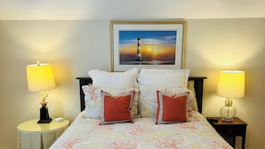 A hotel room with a large bed, two bedside lamps, a framed picture on the wall, and a nightstand with a lamp. - Studio Near the Plantations (Charleston)