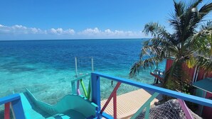 Eine Holzterrasse mit blauer Geländer, die auf klares, türkisblaues Wasser blickt.