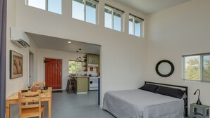 Une chambre spacieuse avec un grand lit, une table à manger avec des chaises, un coin cuisine équipé d’une cuisinière et de placards, et une porte rouge.