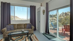 Un salon avec un canapé, une table basse en verre et une vue sur un paysage rocheux grâce à de grandes fenêtres.