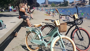 A beach with bicycles parked on the sand, a clear view of the water, and people relaxing in the background. - Walking distance everywhere, yard, front porch and hot tub! (Coeur d'Alene)